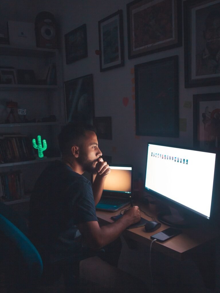 Person focused on computer screen in a dim blue-lit room